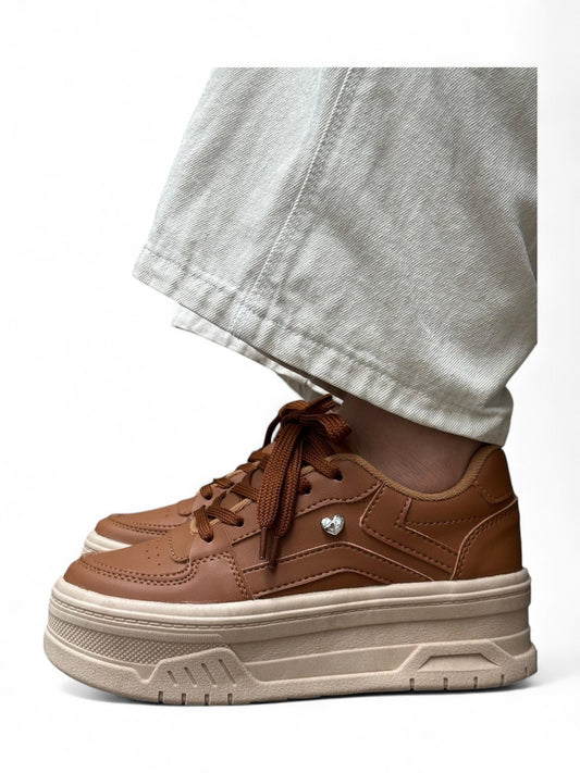 Brown sneakers with white soles worn with light-colored pants on a white background