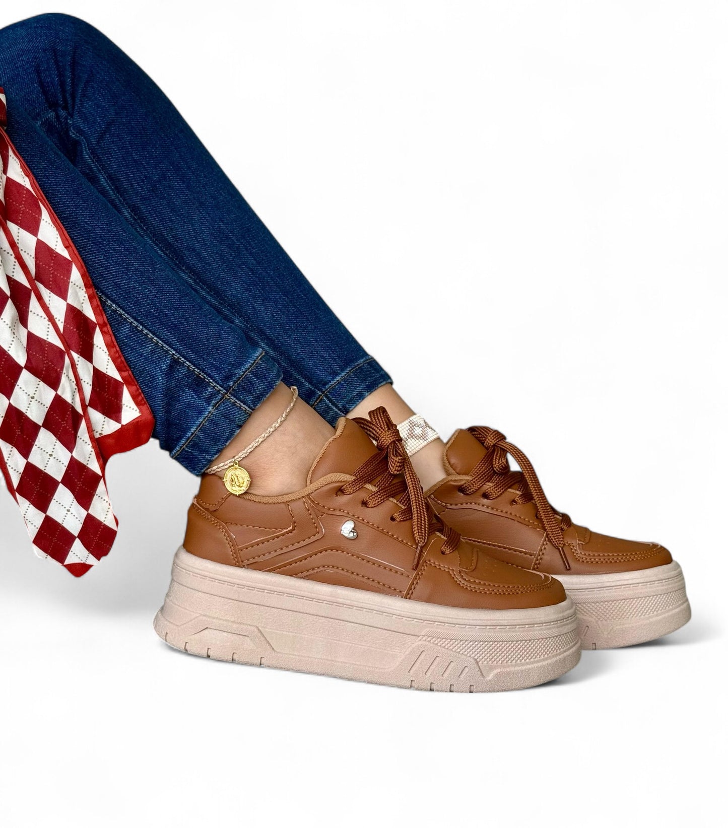 Brown platform sneakers worn with blue jeans and a red checkered fabric on a white background