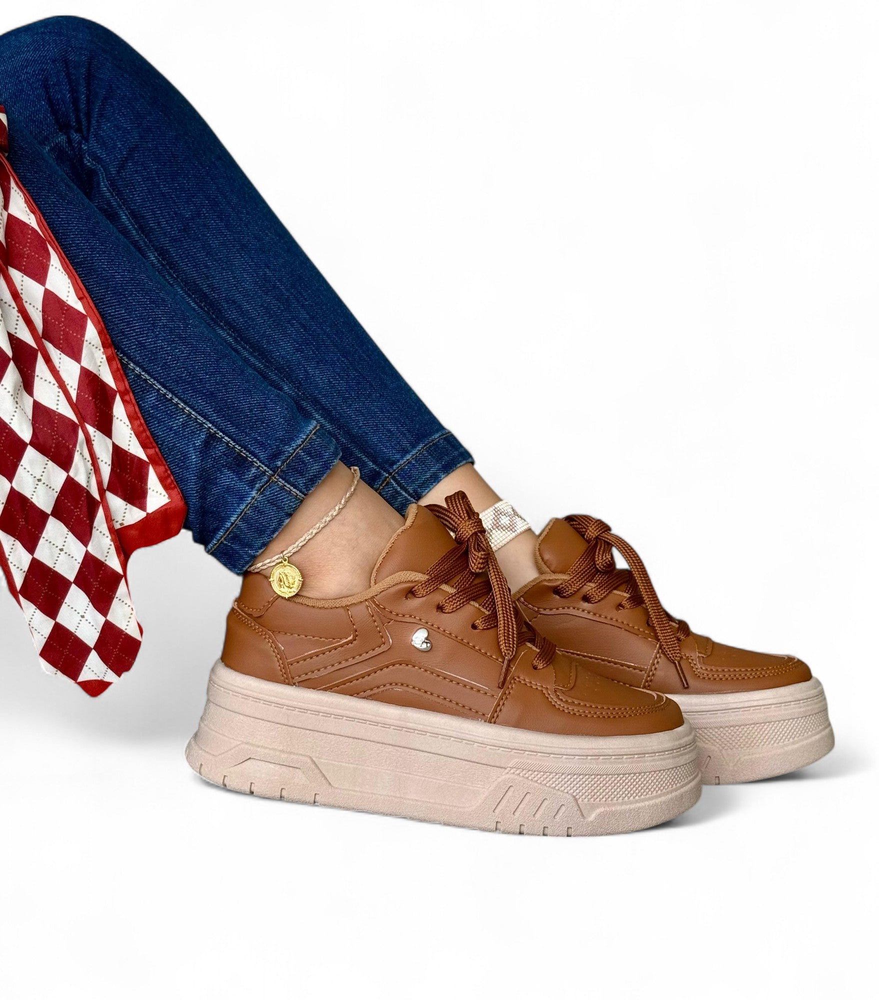 Brown platform sneakers worn with blue jeans and a red checkered fabric on a white background