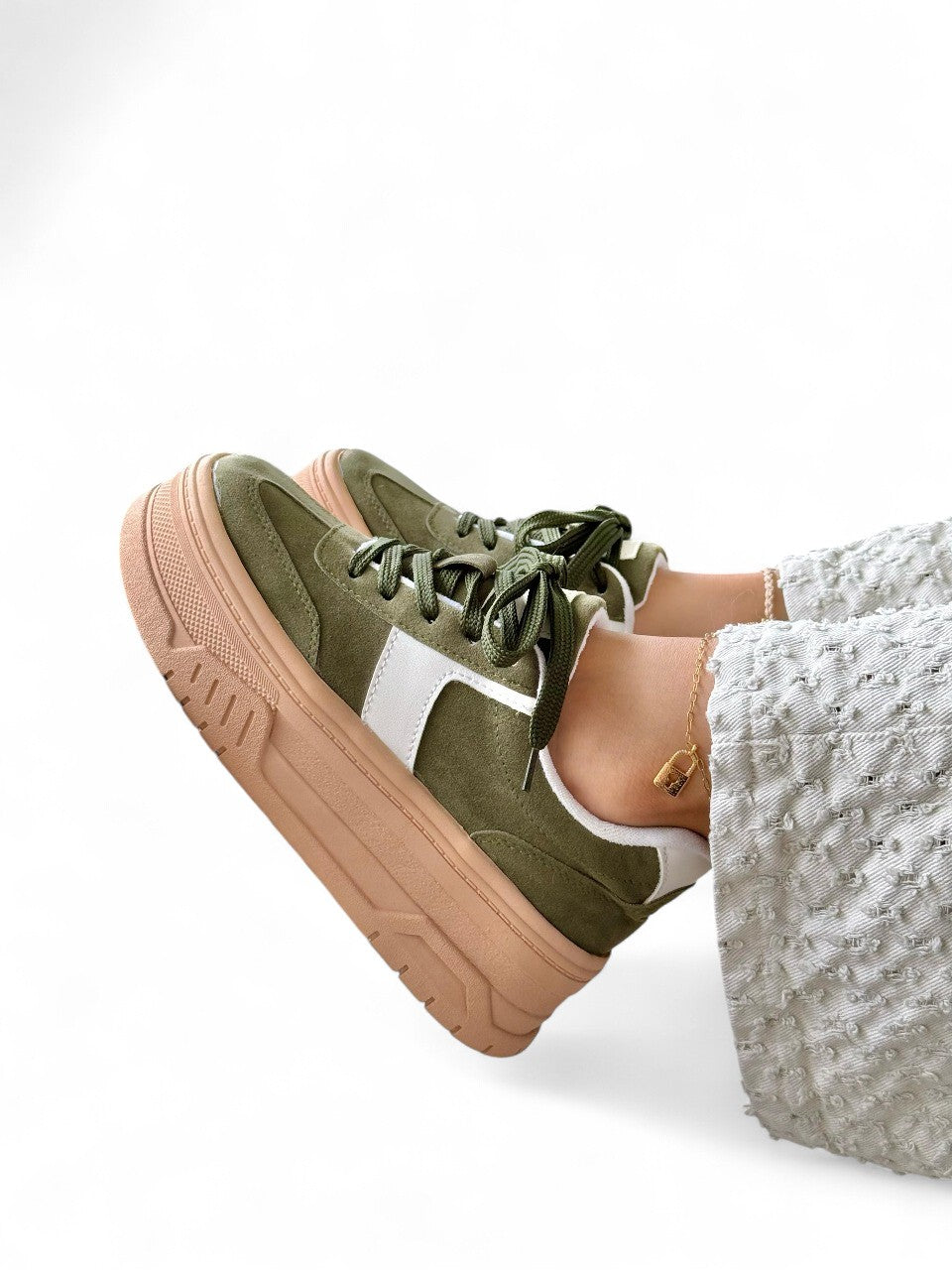 Green sneakers with brown soles worn by a person on a white background