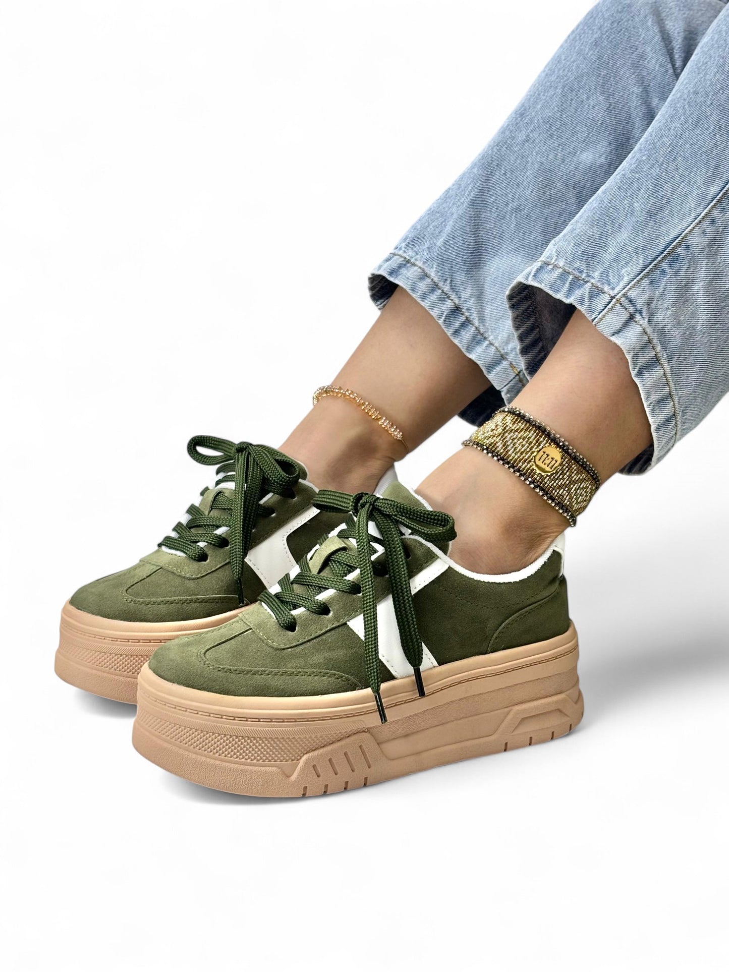Green sneakers with beige soles worn by a person on a white background
