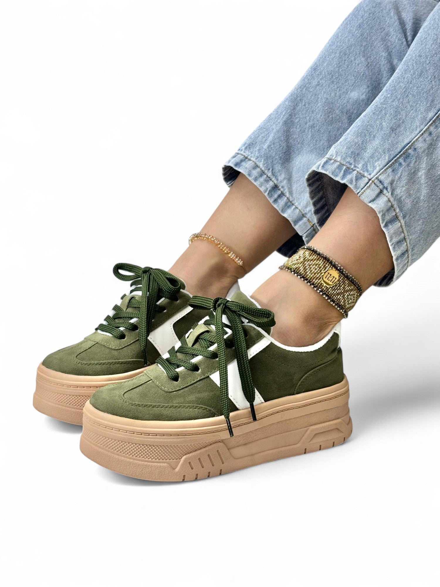 Green sneakers with beige soles worn by a person on a white background