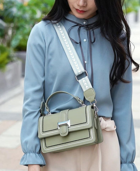 A woman wearing a blue shirt and beige pants is carrying a green handbag with a white strap.
