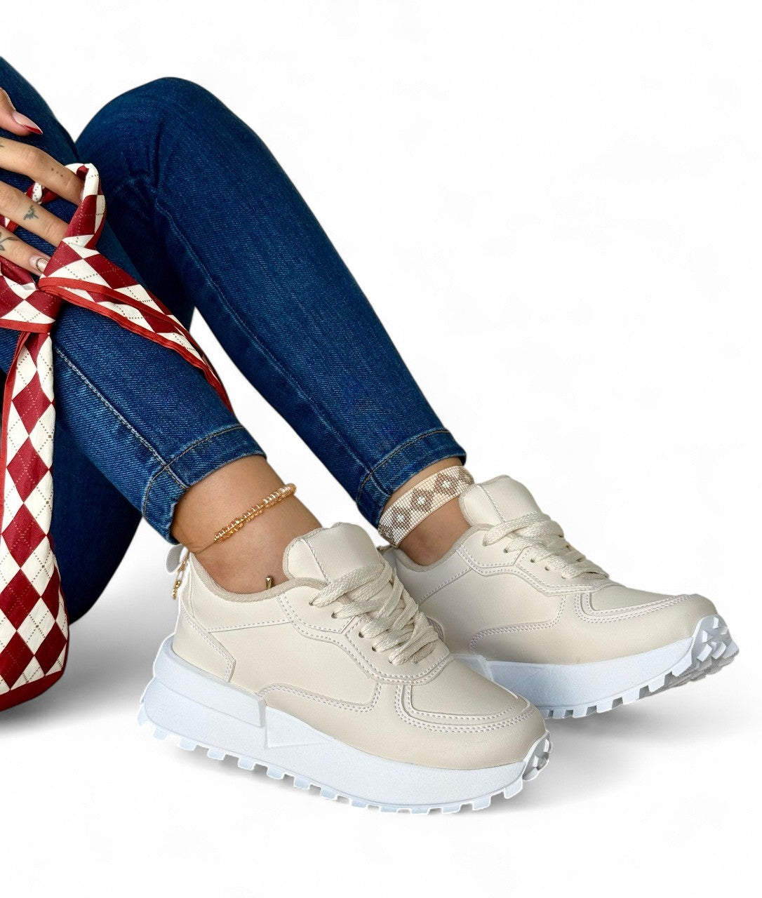 Beige sneakers worn with blue jeans on a white background