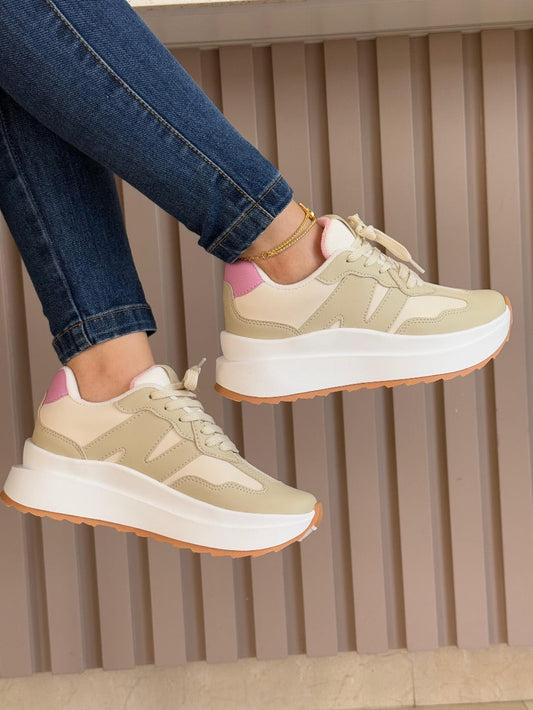 Beige sneakers with pink accents worn with blue jeans on a neutral background