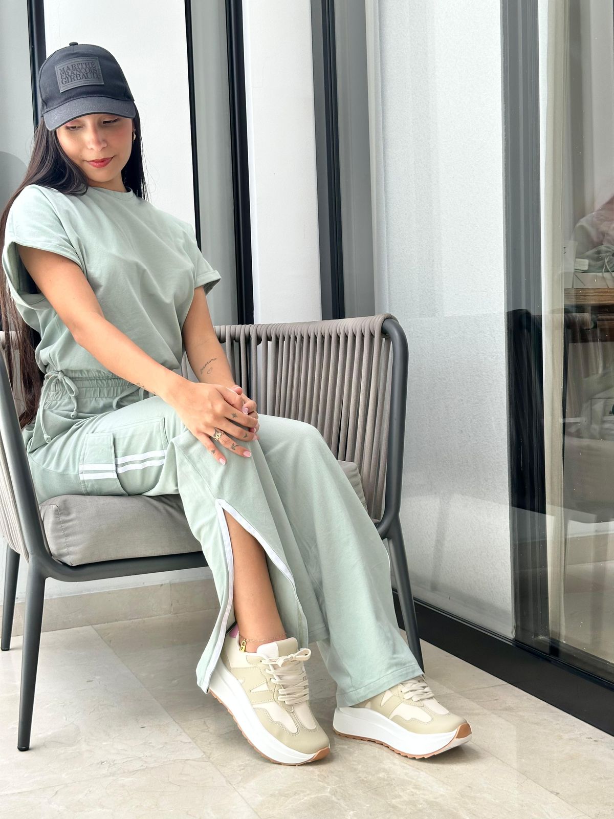 Woman in a light green outfit sitting on a chair indoors using Sneaker America.