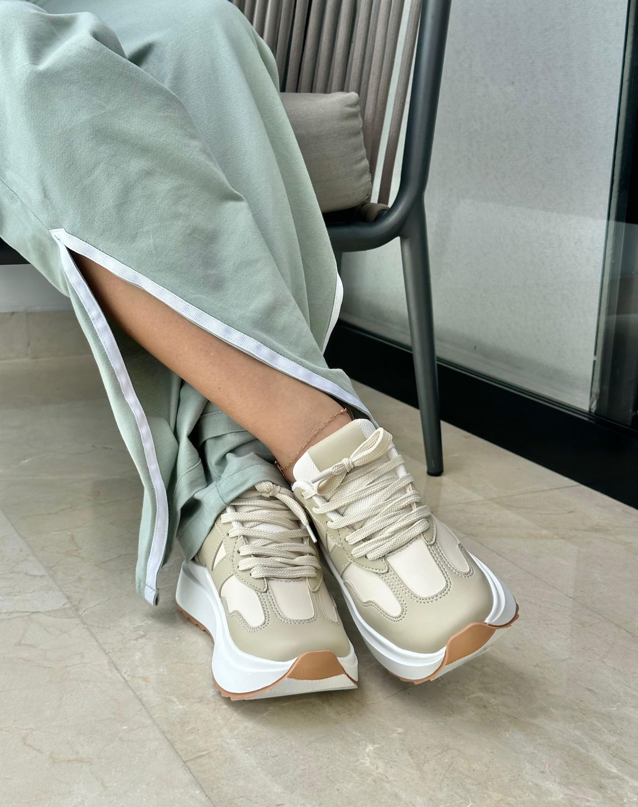 Beige sneakers worn with light green pants on a neutral background