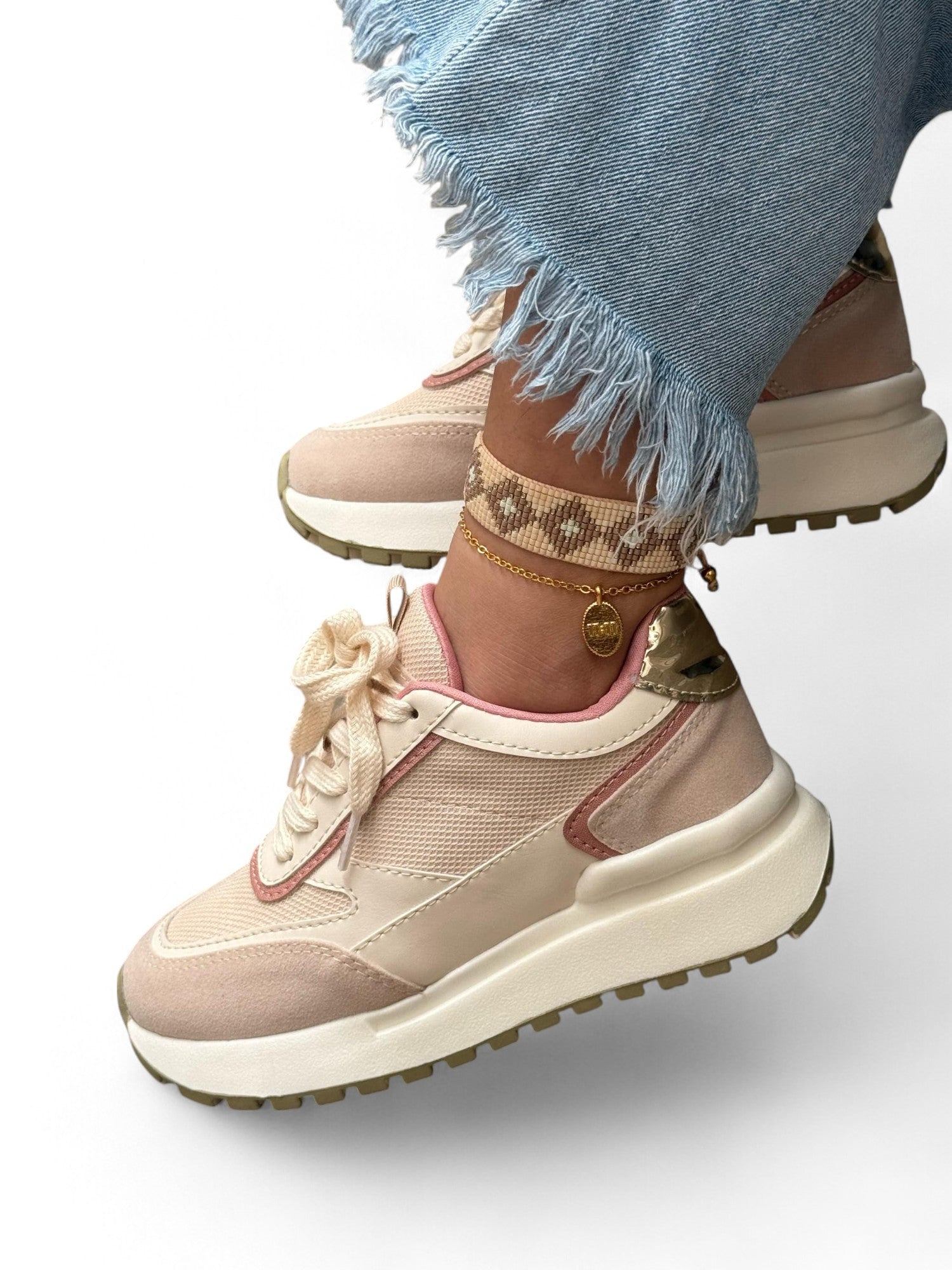 Beige sneakers with decorative elements worn with light blue jeans on a white background