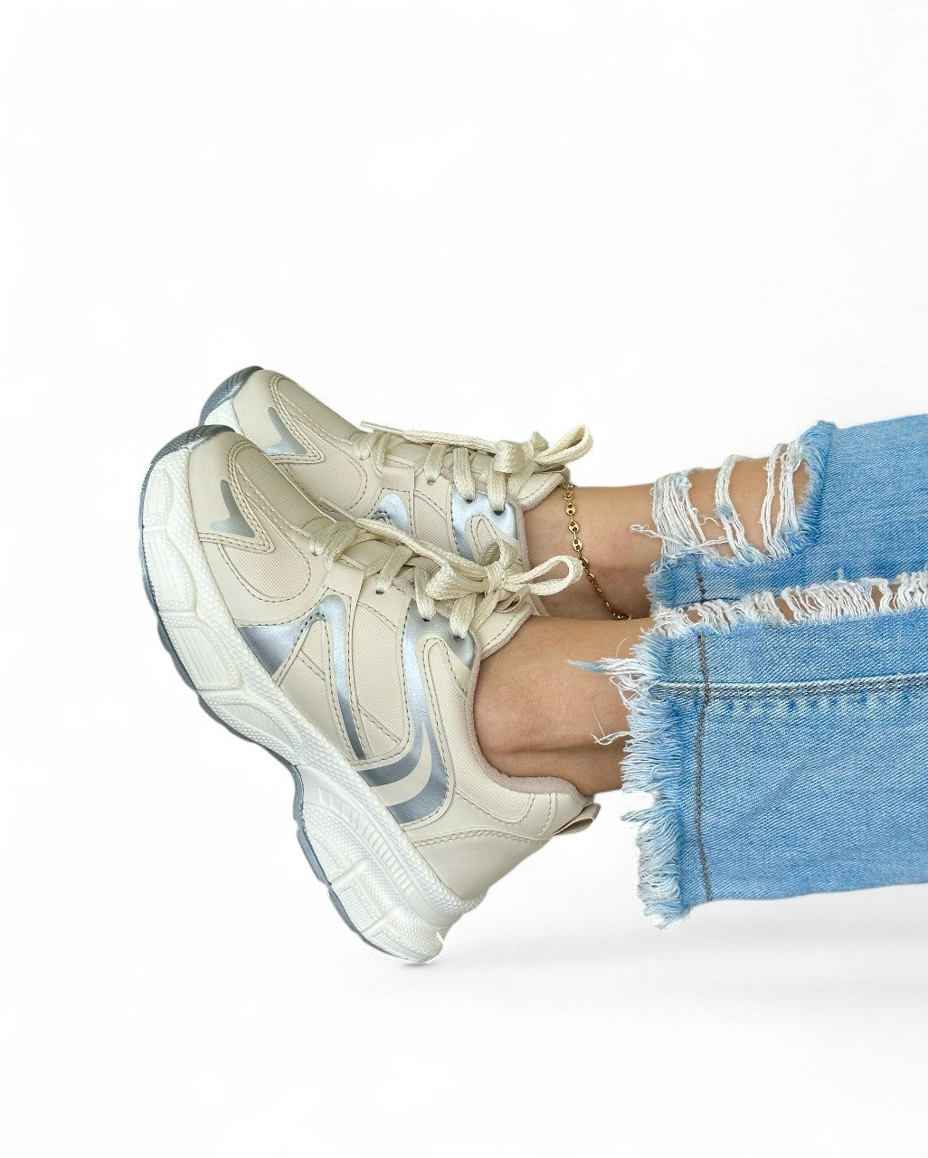 Beige sneakers with white soles worn with ripped blue jeans on a white background