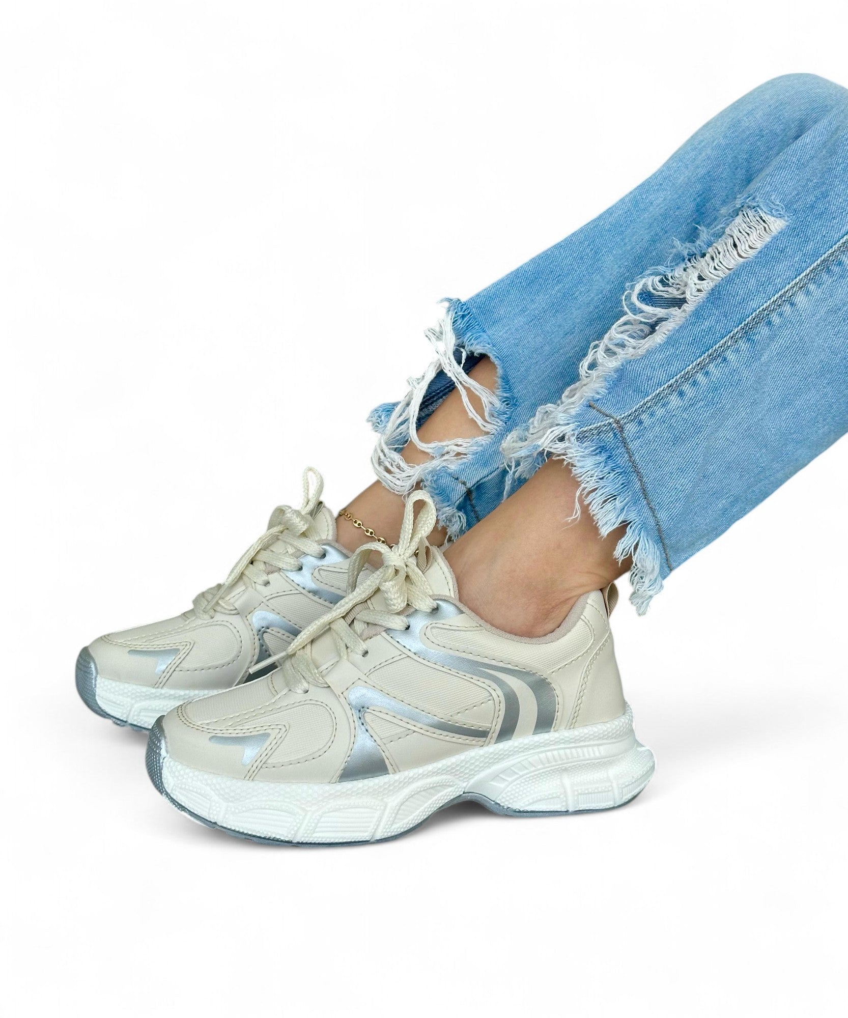 Beige sneakers with white soles worn with light blue jeans on a white background